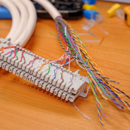 unverkleidetes Endstück einer IP-Telefonie-Leitung auf einem Holztisch; zahlreiche mehrfarbige Leitungen kommen aus dem Kabel.